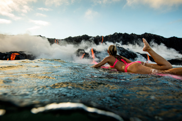 PIC BY PERRIN JAMES / CATERS NEWS - (PICTURED: Alison Teal paddles out to Kilauea volcano in Hawaii as it eruopts into the ocean) - Professional adventurer Alison Teal has become the first woman to paddle out into lava during a volcanic eruption into the sea. Amazing shots of the extreme surf session shows the daredevil riding her pink surfboard up to the base of Kilauea Volcano. Photographer Perrin James snapped the brave explorer within feet of the lava as it flows into the ocean. Its the first the volcano in the Big Island of Hawaii has erupted since 2011. SEE CATERS COPY